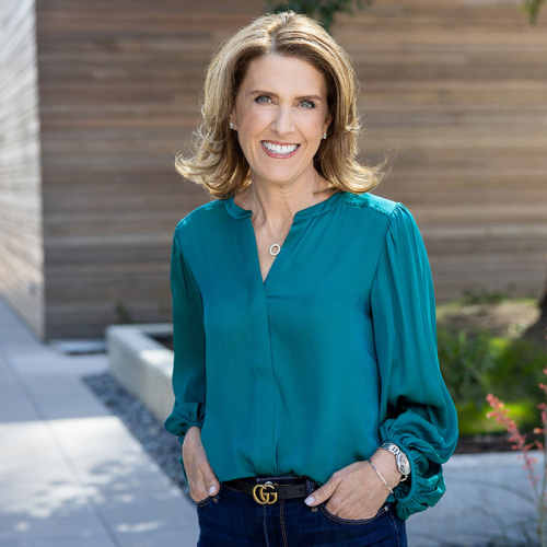 Headshot of Jill Lampert, wearing a teal blouse, with a wooden building in the background