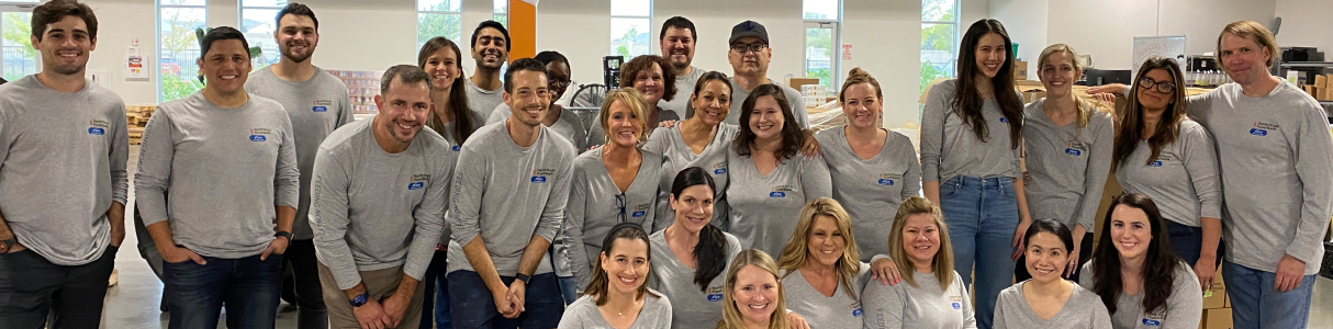 Group of NGP employees all volunteering together and smiling while wearing matching gray, long-sleeved shirts.