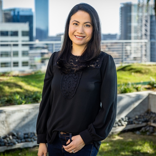 Headshot of Tiffanie Lee, wearing a long-sleeved black blouse, with a city skyline in the background
